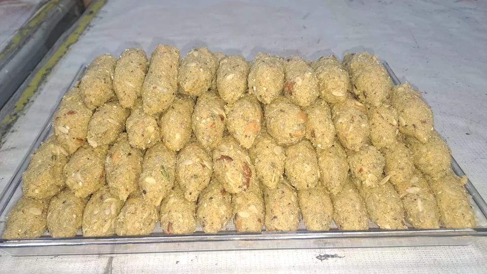 A close view of oval sweets with visible nuts and seeds arranged in rows.