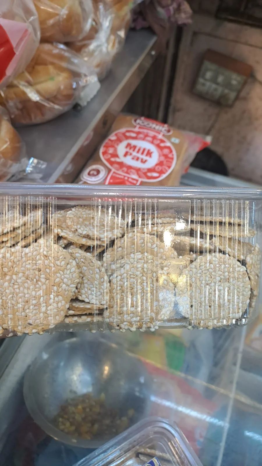 Thin round sesame-coated rewri arranged in a clear rectangular box.