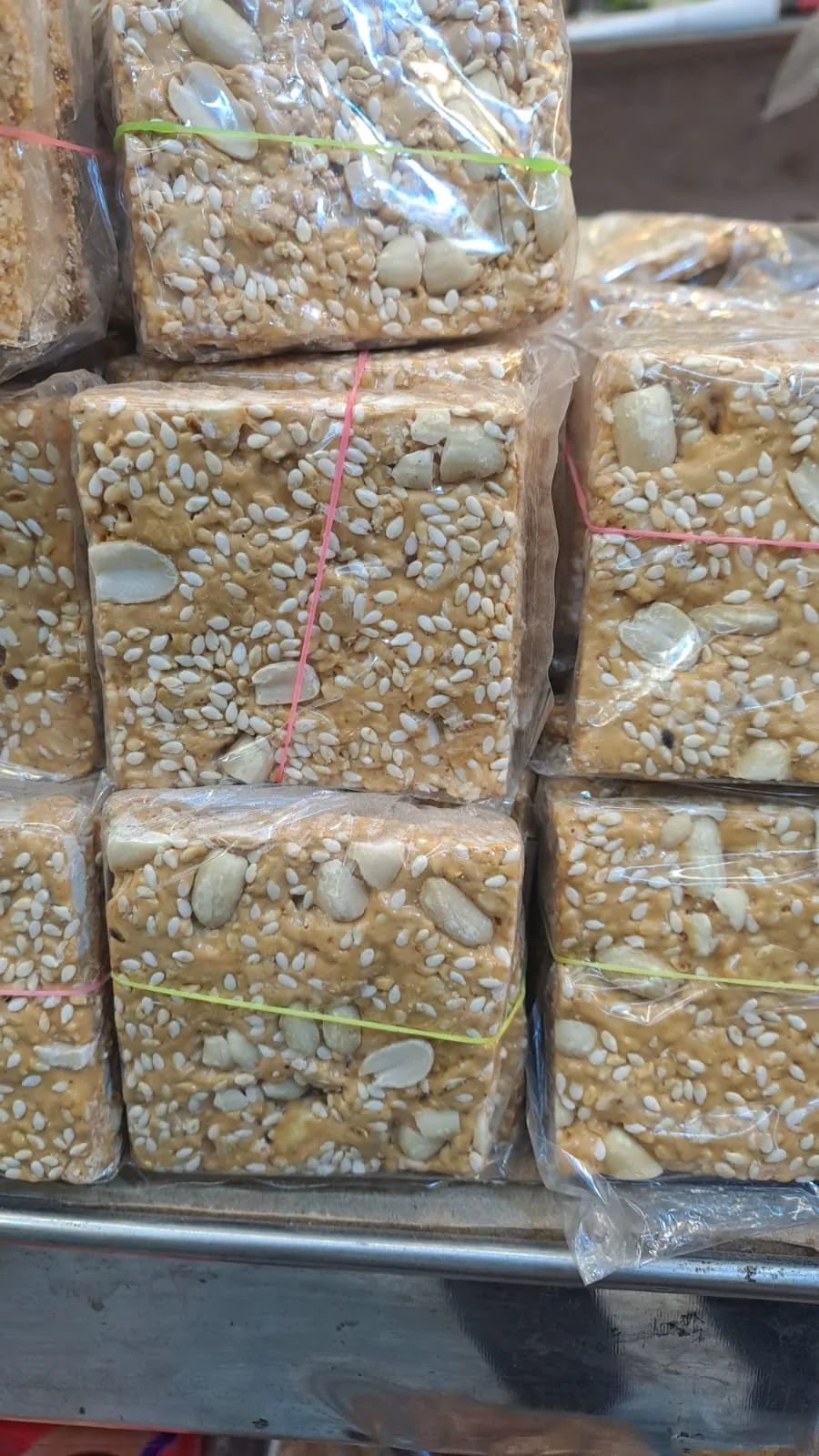 Wrapped sesame chikki blocks topped with cashews.
