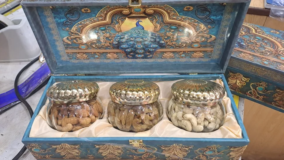 An ornate blue gift box holding three glass jars of dry fruits.