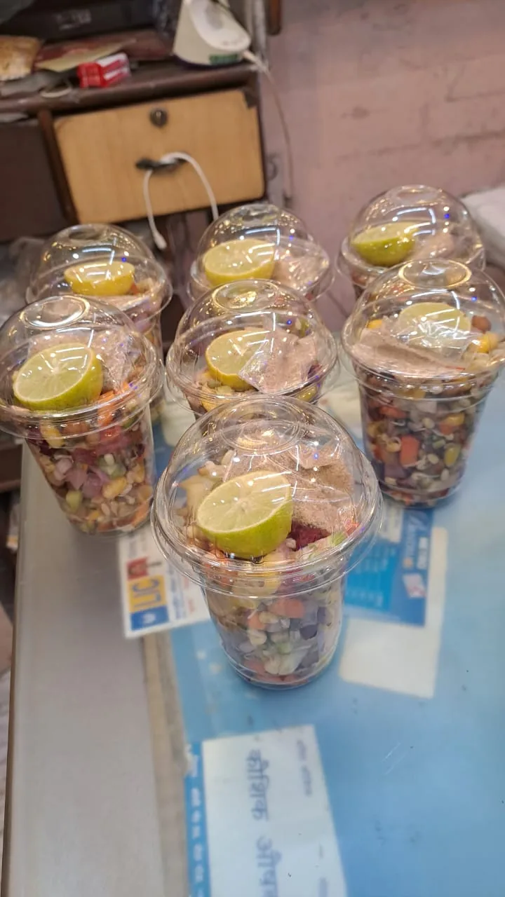 Clear lidded cups of mixed salad with lemon wedges ready on the counter.