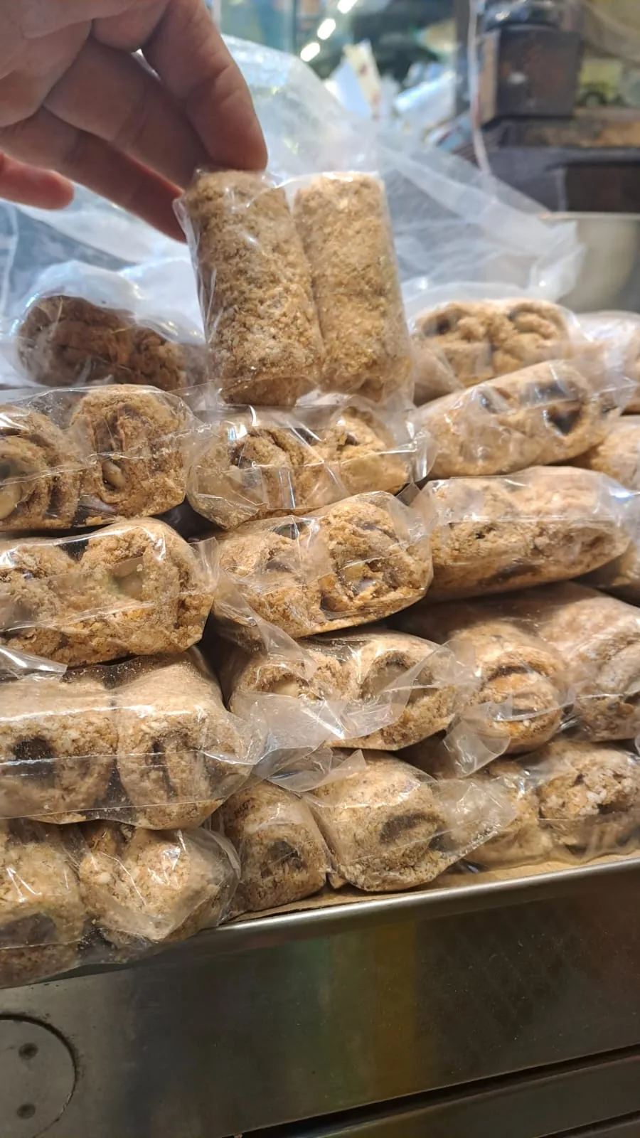 A small wrapped gazak roll held above stacks of packaged rolls.