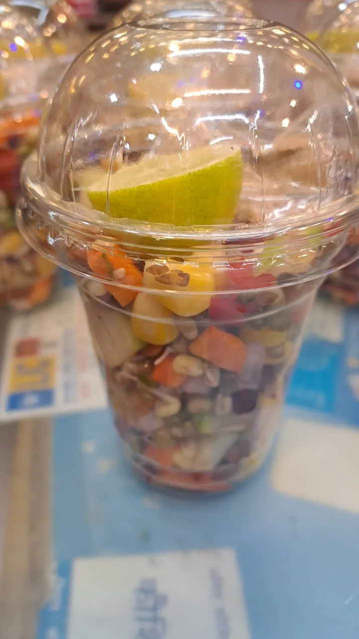 A single takeaway salad cup with vegetables, pulses and a lemon wedge.
