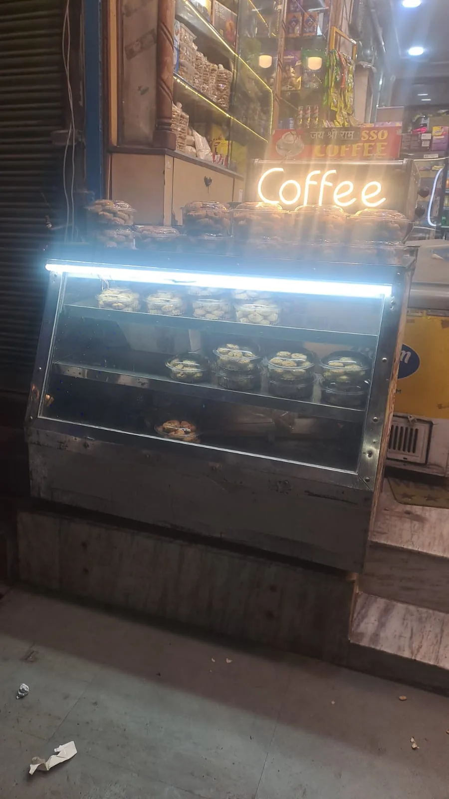 A lit glass display cabinet outside the shop below a coffee sign.