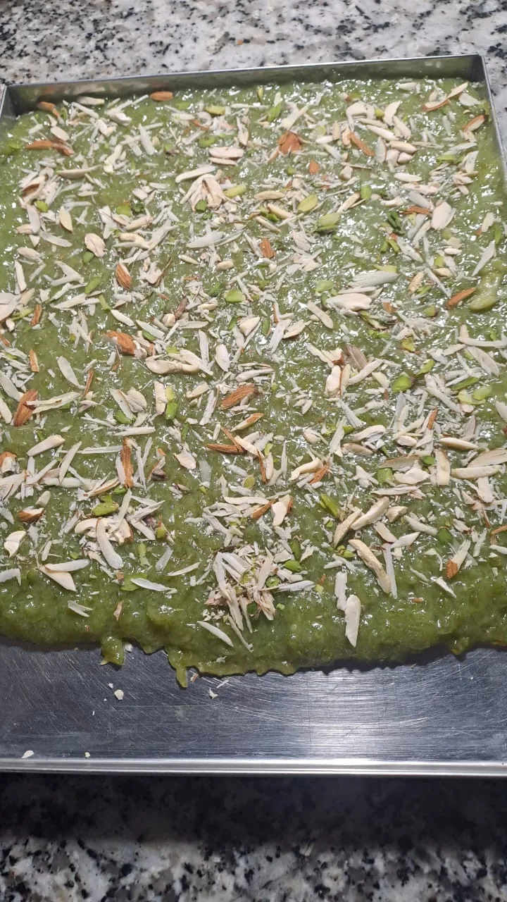 A tray of green halwa garnished with sliced nuts.